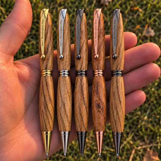 Five wooden ballpoint pens with different metal accents are held in a person's hand outdoors on grass.